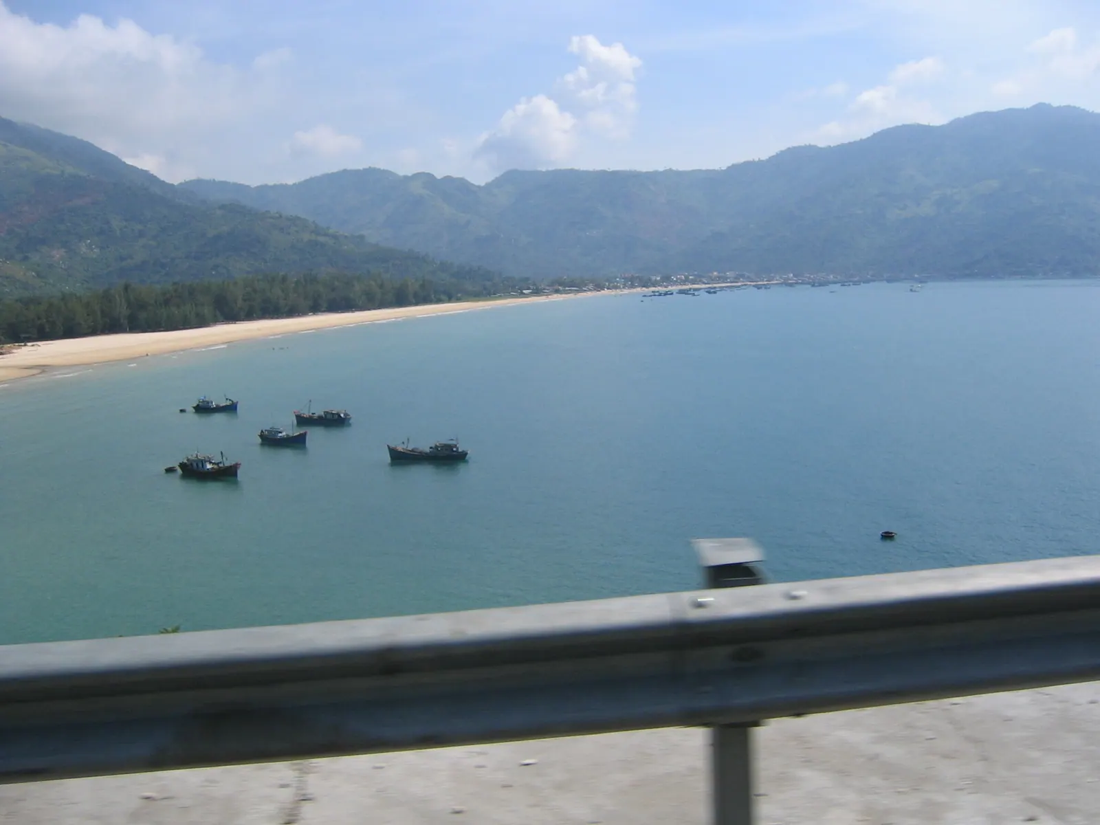 The long curve of Dai Lanh beach with fishing boats offshore and the hills of the Ca pass behind