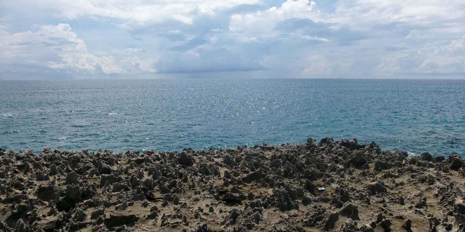 The ancient coral reef platform at Hang Rai exposed at low tide, with terraces of pitted rock at the water's edge