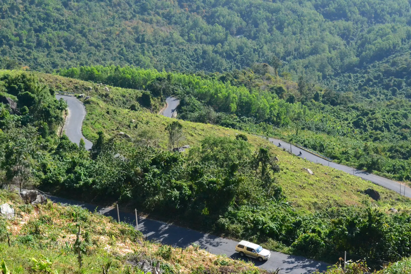 The switchbacks of the Khanh Son pass road winding down through green hills.