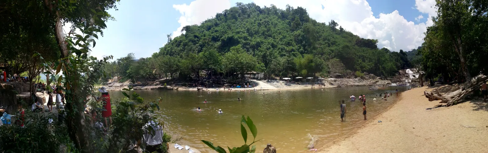 A rocky river bend in Khanh Phu commune, Khanh Vinh, with people bathing below forested hills
