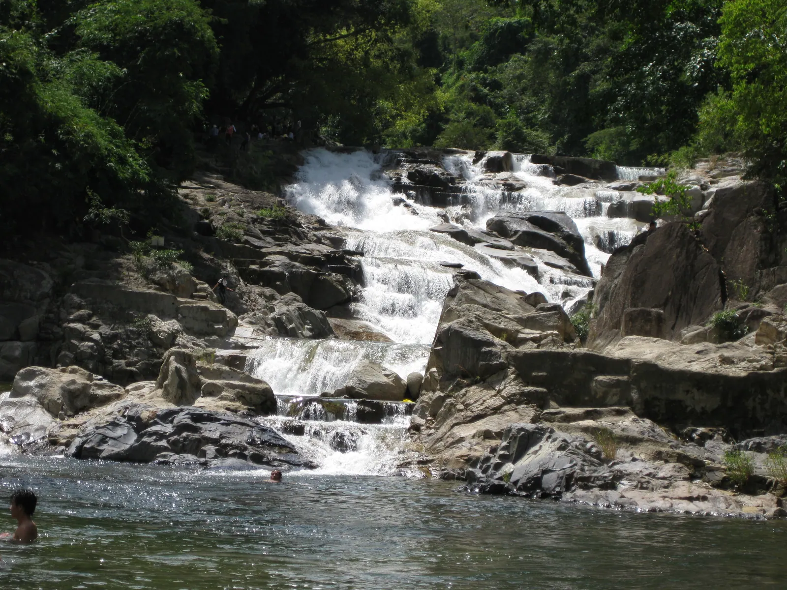 Visitors at the foot of the Yang Bay waterfall, which drops in white steps through the forest